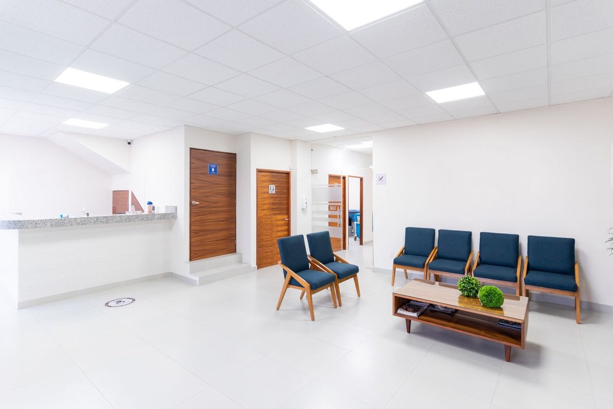 Bright clinic waiting room with navy chairs, a glass-top coffee table, and a white reception counter