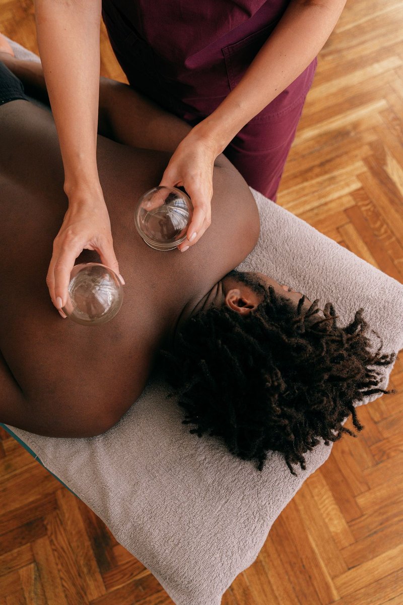 Therapist's hands placing glass cupping cups on the back of a person lying on a mat